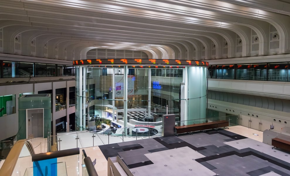 The main room of the Tokyo Stock Exchange, with a circular glass market centre under a ring of ticker displays and a vaulted white ceiling