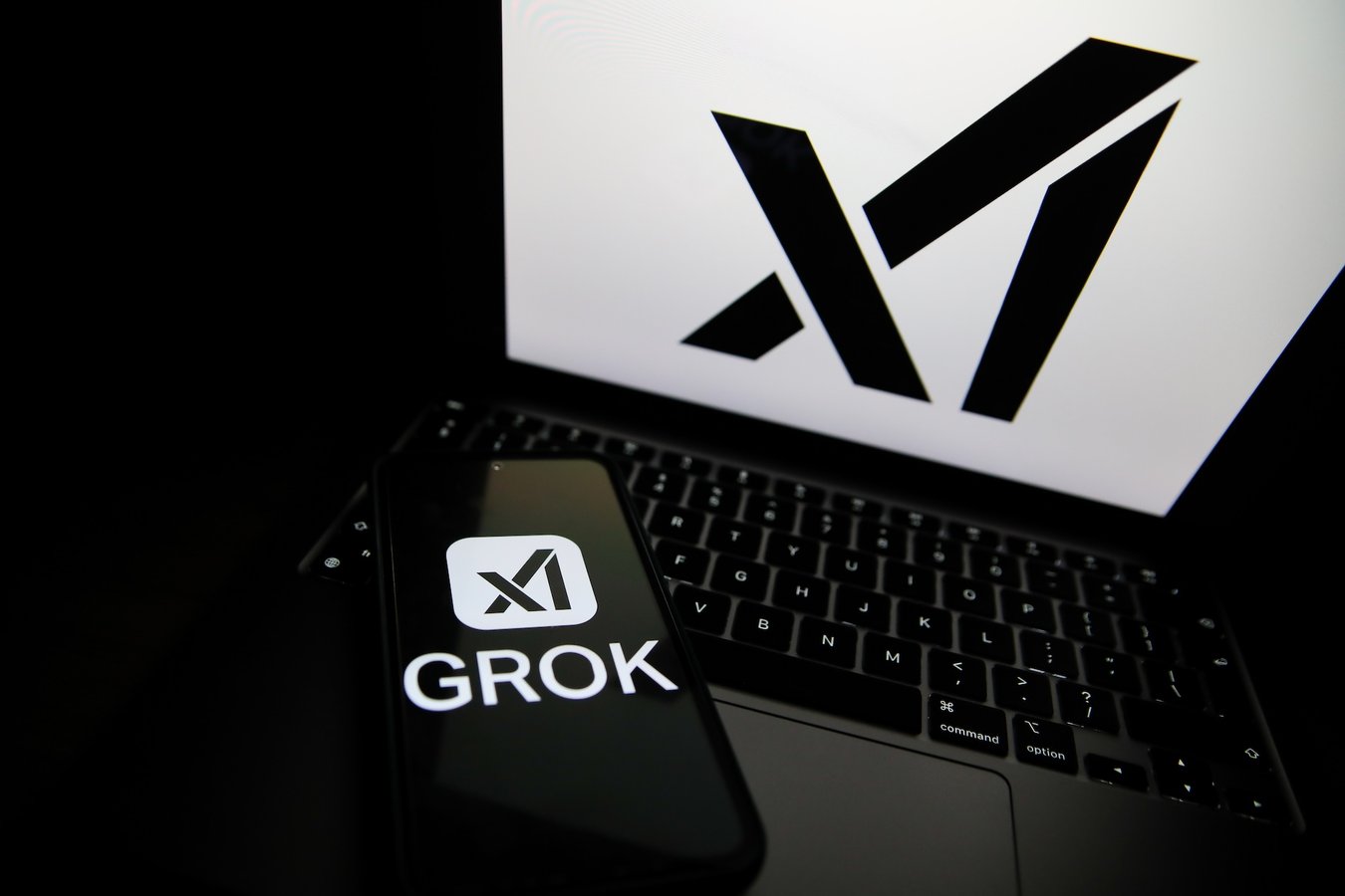 Grok logo displayed on a smartphone next to a laptop showing the xAI logo
