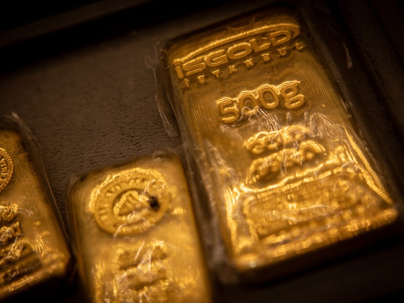 A gold bar held up against a blurred trading floor background as markets weigh the Fed rate hike and oil price decline