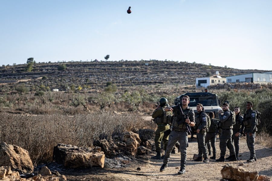 Israeli security personnel stand on a dirt track near olive terraces as a tear gas grenade flies through the air in Abu Falah, West Bank