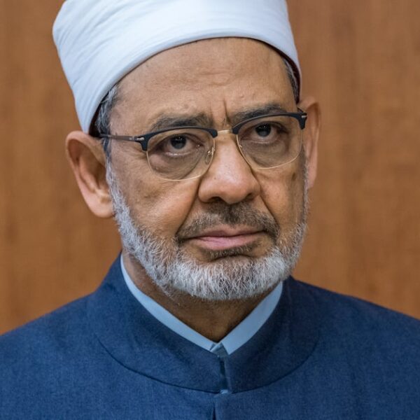 Portrait of Al-Azhar Grand Imam Ahmed Al Tayeb in a white turban and glasses against a wood-panelled wall