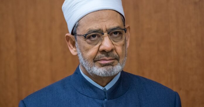 Portrait of Al-Azhar Grand Imam Ahmed Al Tayeb in a white turban and glasses against a wood-panelled wall