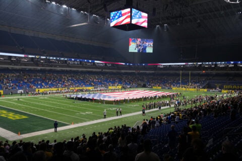 Interior of the Alamodome in San Antonio with a large American flag unfurled on the field and a color guard shown on the video board