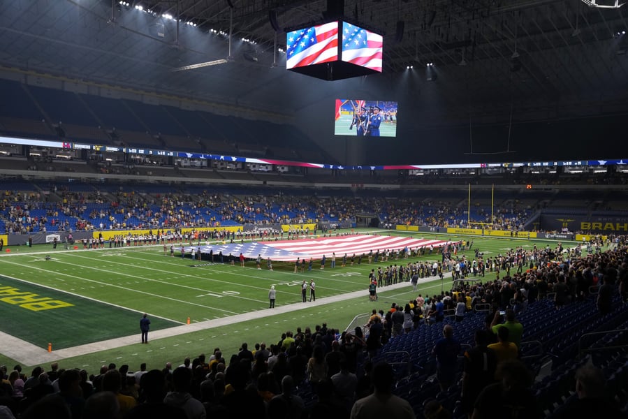 Interior of the Alamodome in San Antonio with a large American flag unfurled on the field and a color guard shown on the video board