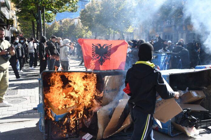 Masked protesters stand behind a burning rubbish container and an Albanian flag during anti-government protests in Tirana