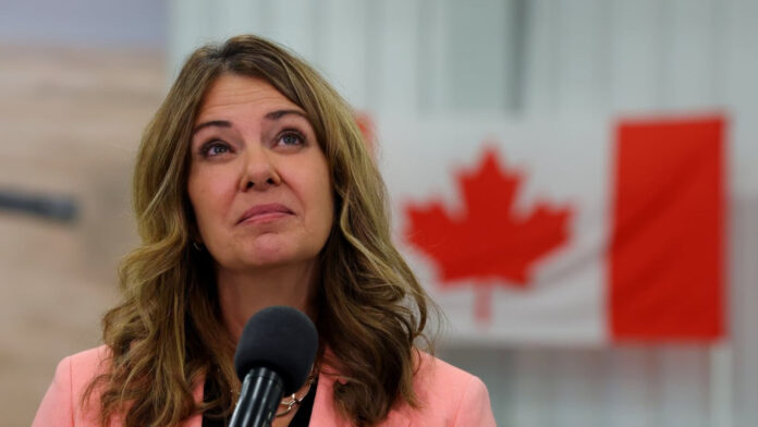 Alberta Premier Danielle Smith speaking at a microphone in front of a Canadian flag