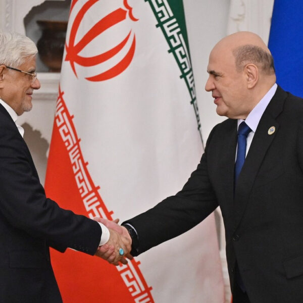 Iranian First Vice President Mohammad Reza Aref and Russian Prime Minister Mikhail Mishustin shake hands in front of Iranian and Russian flags