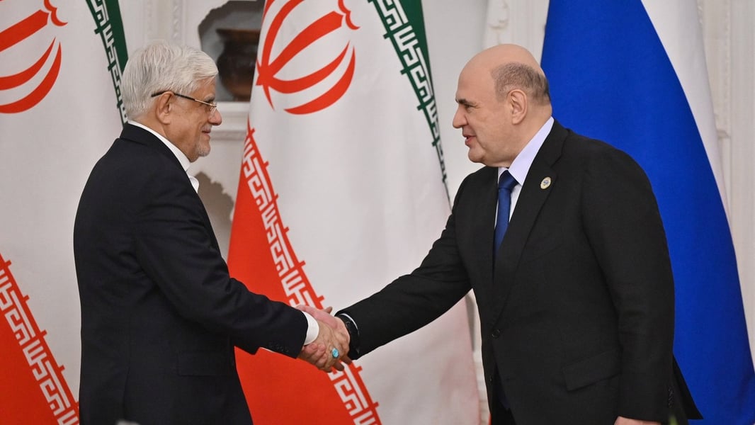 Iranian First Vice President Mohammad Reza Aref and Russian Prime Minister Mikhail Mishustin shake hands in front of Iranian and Russian flags