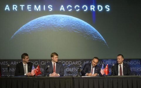 Türkiye's industry and technology minister signs the Artemis Accords at a table with US and Turkish flags beneath a Moon image and the words Artemis Accords
