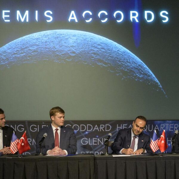 Türkiye's industry and technology minister signs the Artemis Accords at a table with US and Turkish flags beneath a Moon image and the words Artemis Accords