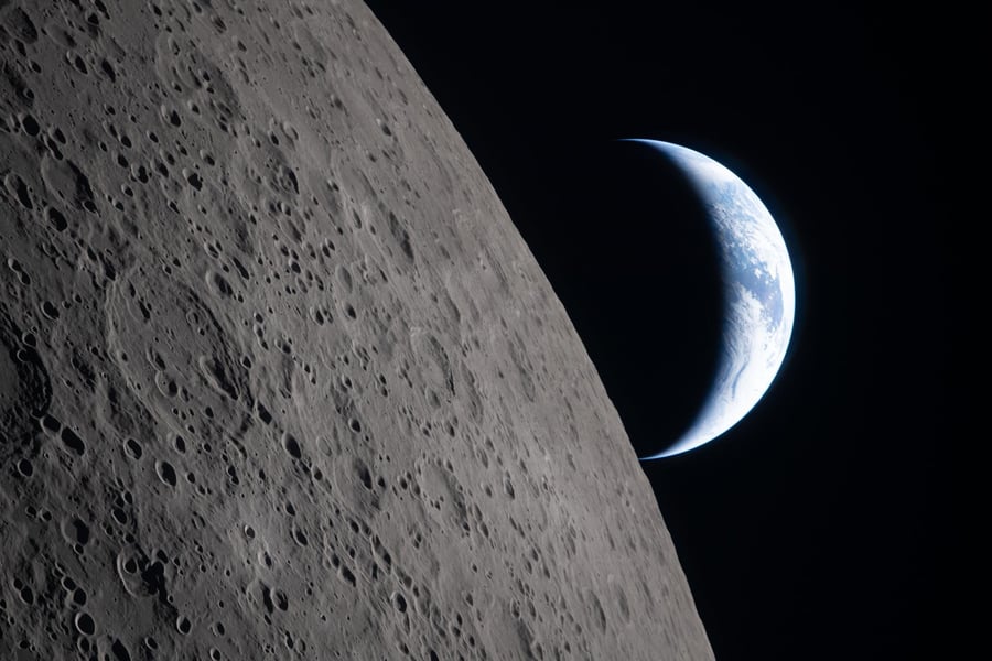 A crescent Earth sets behind the edge of the cratered Moon in a photograph taken by the Artemis II crew