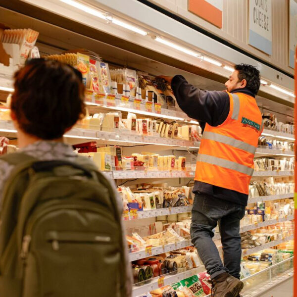 A supermarket worker arranging goods on a shelf in Canberra as a shopper passes