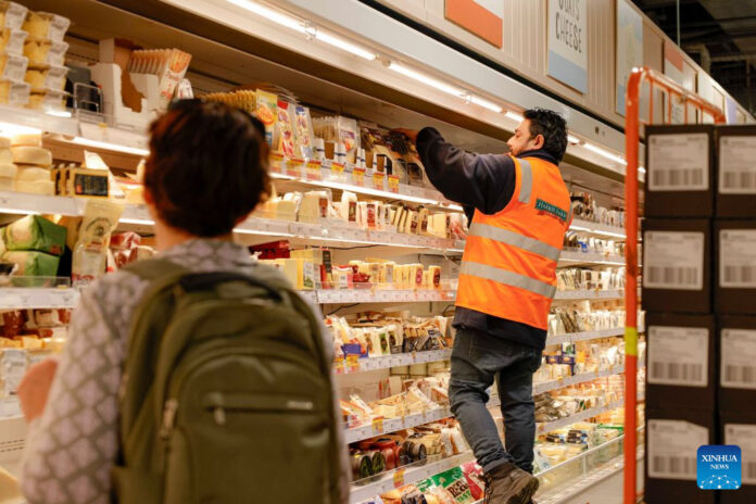 A supermarket worker arranging goods on a shelf in Canberra as a shopper passes