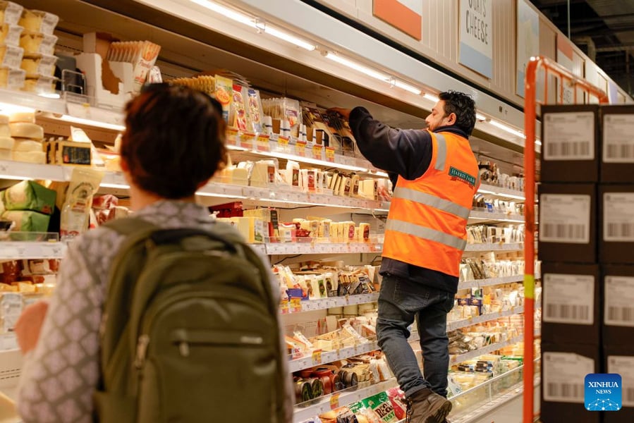 A supermarket worker arranging goods on a shelf in Canberra as a shopper passes