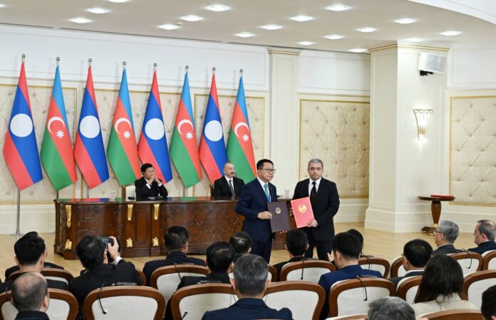 Officials exchange signed documents in front of Azerbaijani and Lao flags as Presidents Aliyev and Thongloun look on in Baku