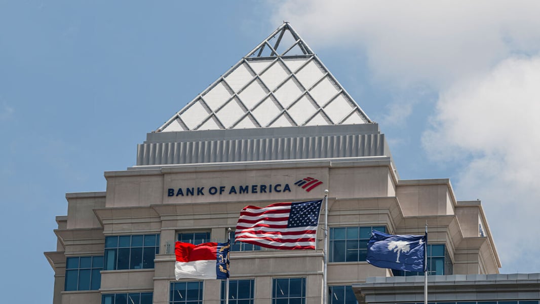Bank of America signage below a glass pyramid roof on a Charlotte, North Carolina building with US and state flags in front