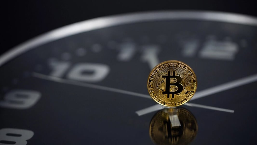 A gold bitcoin coin standing upright on a dark clock face