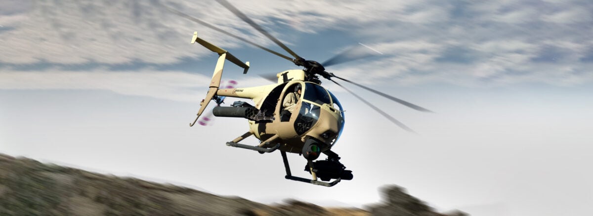 A tan Boeing AH-6 Little Bird helicopter banking low over a ridge with a sensor turret under the nose