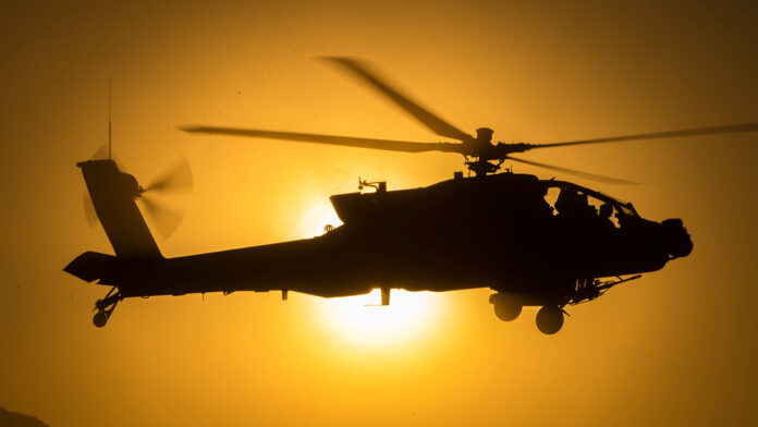 A Boeing AH-64 Apache attack helicopter hovering in front of a desert mesa