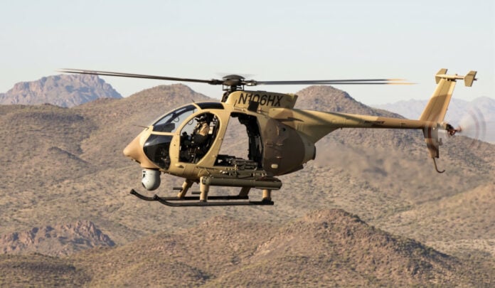 A tan Boeing AH-6i light attack helicopter in flight over desert hills