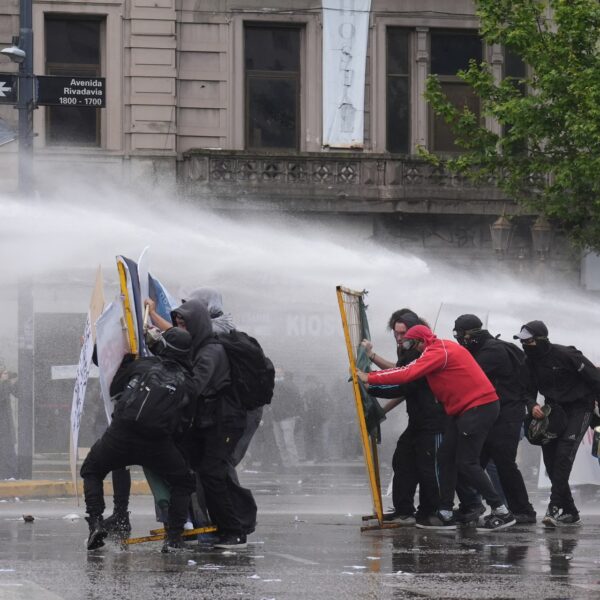 Hooded protesters crouch behind makeshift shields as a water cannon sprays them on a Buenos Aires street