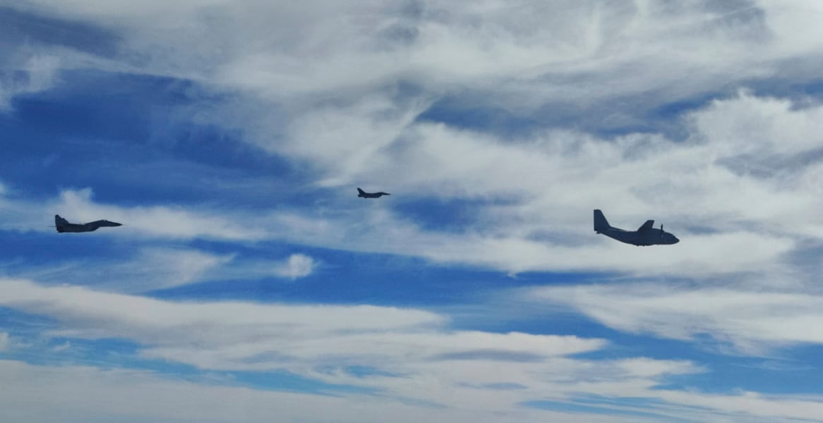 Two fighter jets and a twin-propeller transport aircraft flying in formation against a cloudy blue sky