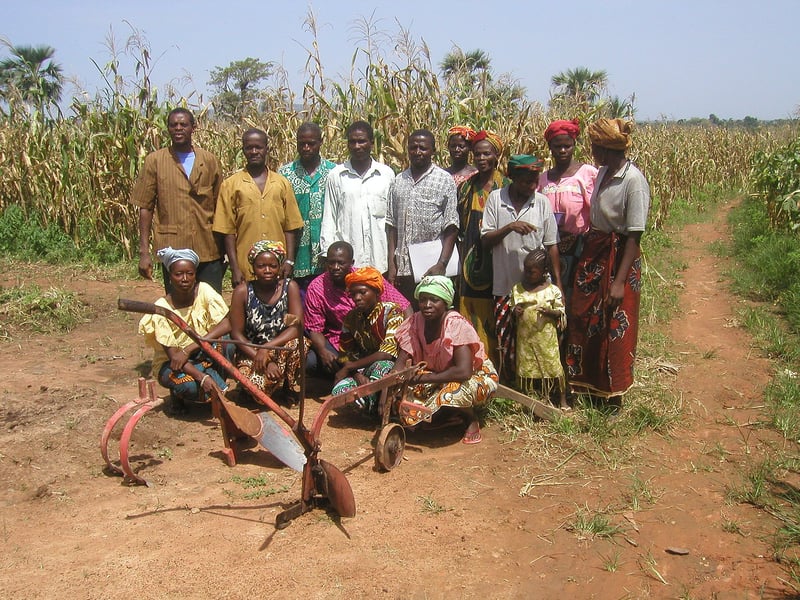 Farmers, women and children standing in a cornfield in Burkina Faso with two traditional plows in the foreground
