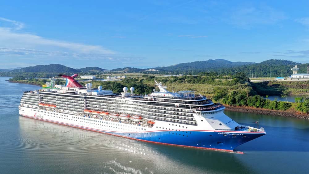 The cruise ship Carnival Miracle passes through the Panama Canal with green hills behind it