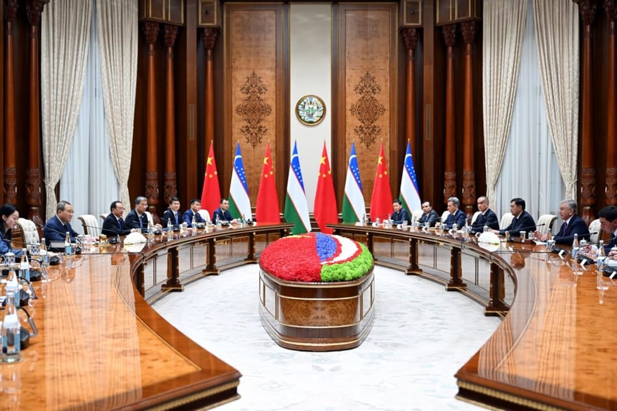Chinese and Uzbek delegations seated across a long table with flags behind them during talks on October 17