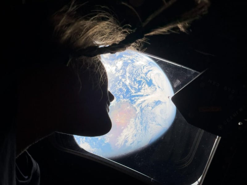 NASA astronaut Christina Koch in silhouette looking at Earth through a window of the Orion spacecraft during Artemis II
