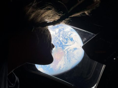 NASA astronaut Christina Koch in silhouette looking at Earth through a window of the Orion spacecraft during Artemis II