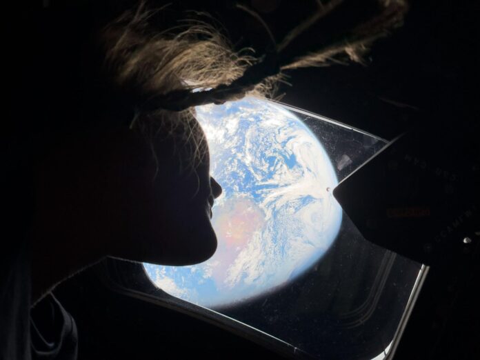 NASA astronaut Christina Koch in silhouette looking at Earth through a window of the Orion spacecraft during Artemis II