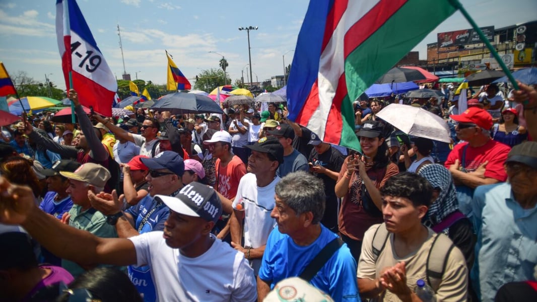A dense crowd of protesters under umbrellas and flags at a demonstration in Colombia