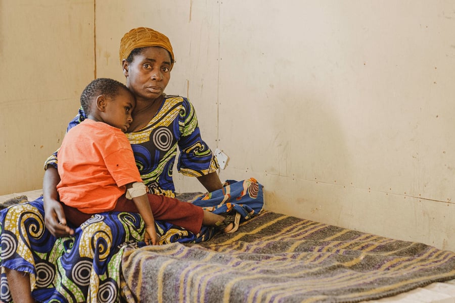 A woman in a patterned dress holds a young child on a bed at a cholera treatment centre in South Kivu