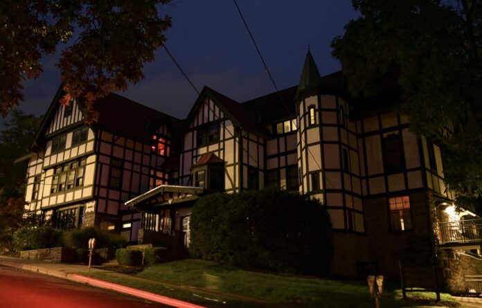 The Chi Phi fraternity house in Ithaca, New York, a half-timbered building lit at night with a few windows glowing