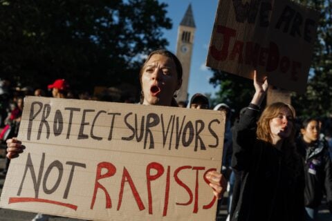 A protester holds a Protect Survivors sign in front of the Cornell clock tower in Ithaca