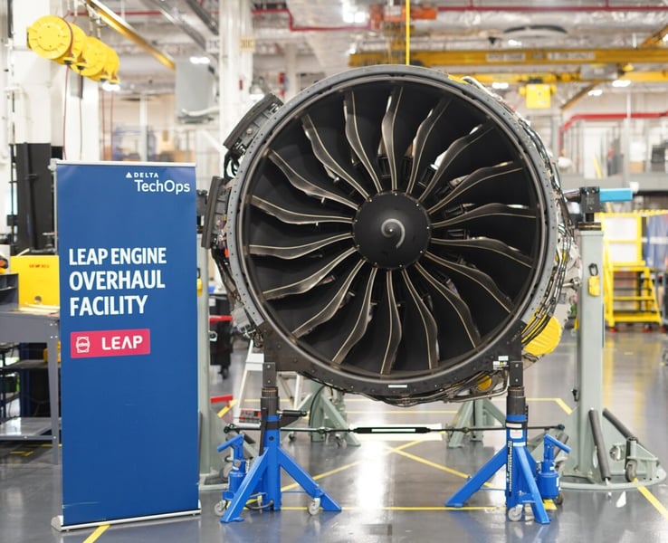 A LEAP-1B jet engine on stands beside a Delta TechOps LEAP Engine Overhaul Facility banner
