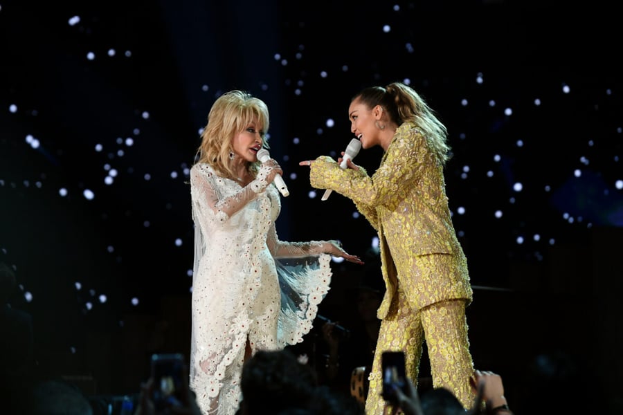 Dolly Parton and Miley Cyrus sing into microphones facing each other on the Grammy Awards stage in 2019