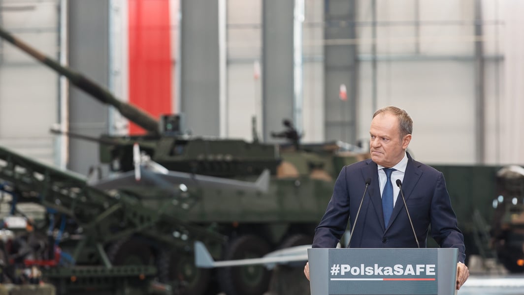 Polish Prime Minister Donald Tusk at a lectern marked PolskaSAFE in front of armoured vehicles