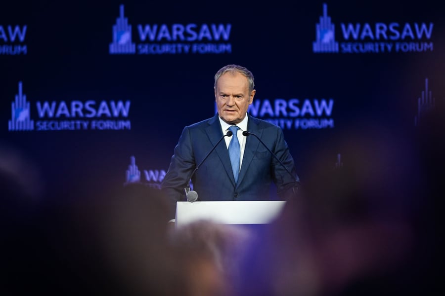 Polish Prime Minister Donald Tusk speaking at a lectern in front of Warsaw Security Forum banners