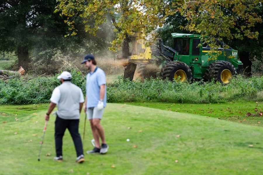 A tree-cutting machine works behind two golfers at East Potomac Golf Links in Washington