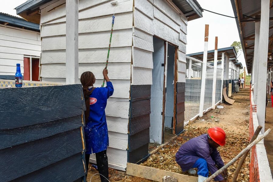 A construction worker paints the white wooden wall of a new Ebola treatment centre in Rwankole, Ituri, while another works on the ground