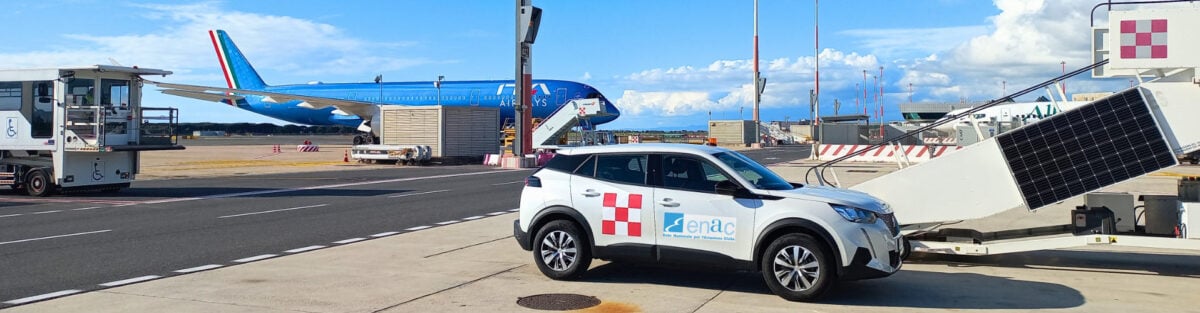 A white ENAC vehicle on an airport apron beside an ITA Airways jet