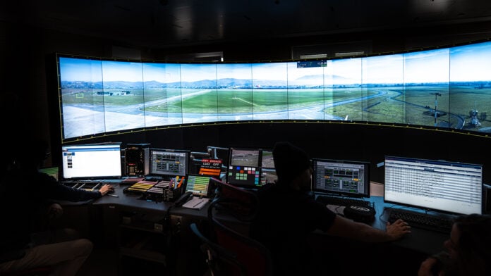 Air traffic controllers at workstations facing a panoramic screen showing an airfield in an ENAV remote tower control room