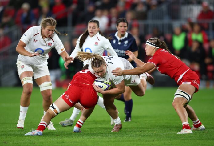 An England ball-carrier is tackled by two Canada defenders in a WXV Global Series match between the Red Roses and Canada