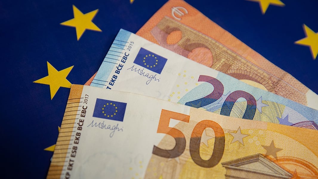 Fifty, twenty and ten euro banknotes fanned out over a blue European Union flag with yellow stars