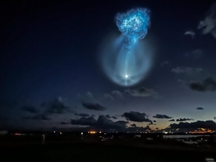 A glowing blue jellyfish-shaped exhaust plume from the Falcon 9 second stage in the pre-dawn sky over Florida