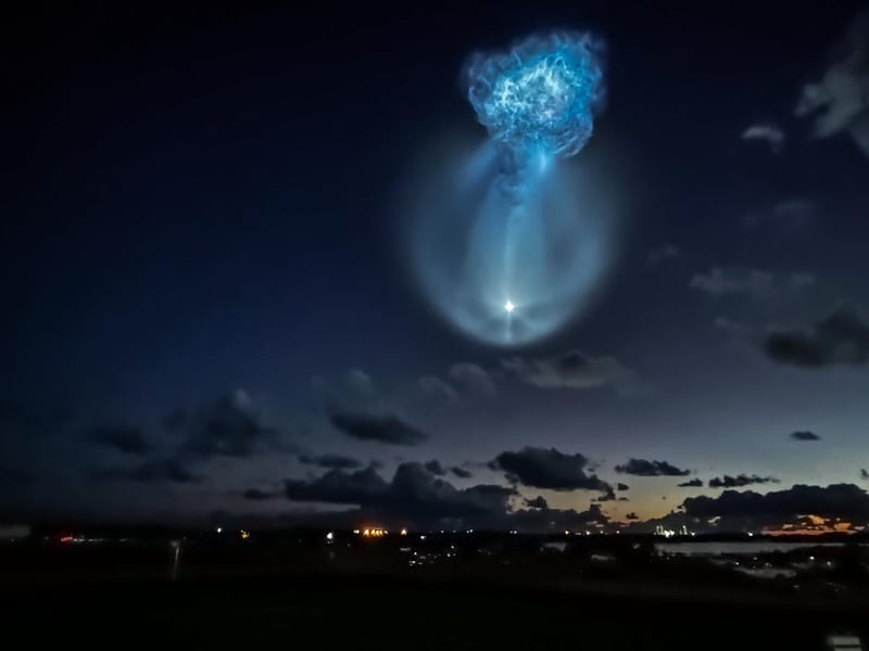 A glowing blue jellyfish-shaped exhaust plume from the Falcon 9 second stage in the pre-dawn sky over Florida