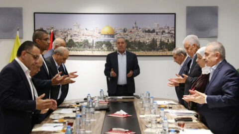 Members of the Fatah Central Committee standing with hands raised in prayer around a meeting table in Ramallah