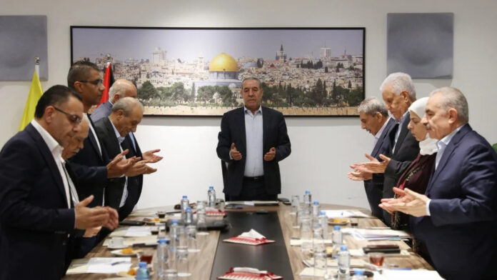 Members of the Fatah Central Committee standing with hands raised in prayer around a meeting table in Ramallah